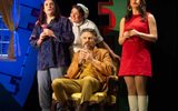 Professor Plum, Mrs White and Miss Scarlett (Ellie Leach) stand around a seated Colonel Mustard (Jason Durr)