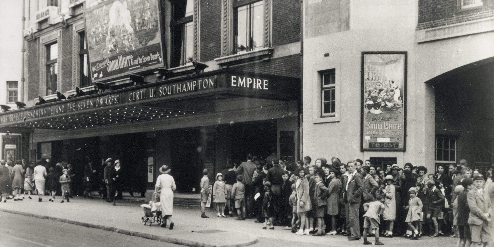 An old black and white photo of people queueing outside the Empire waiting to see the animated film Snow White and the Seven Dwarfs.