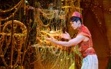 Aladdin (Gavin Adams) reaches to lift a golden lamp from a pile of golden treasure.