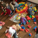 Birds-eye view of young children playing with brightly coloured toys on a hard wood floor.