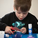 A young oy cutting card with scissors during an arts and craft session at our Family Fun Day.