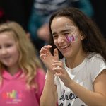 A young girl with a butterfly painted on the left side of her face. She has her hands raised and is laughing.