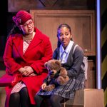 A woman wearing a red coat and red hat sits with a school girl clutching a teddy bear.