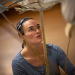 A woman wearing a stripy blue and white top and a blue bandana holds a puppet made from bamboo sticks.