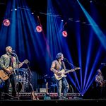 The Illegal Eagles on stage, 3 guitar players singing into microphones, drums behind them