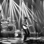 Black and white photo of The Illegal Eagles playing guitar on stage, drums behind them