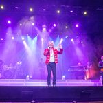 Rod Stewart impersonator in red military jacket singing on purple lit stage