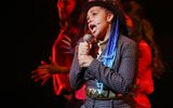 Young female performer wearing a suit and tie, singing into a microphone in our 2021 Summer Youth Project, The Lightning Thief The Percy Jackson Musical.