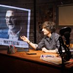 Danny Robins sits at a wooden desk with a flip phone open before him, a polaroid of a middle-aged white man with glasses labelled Matthew projected on the wall to his side.