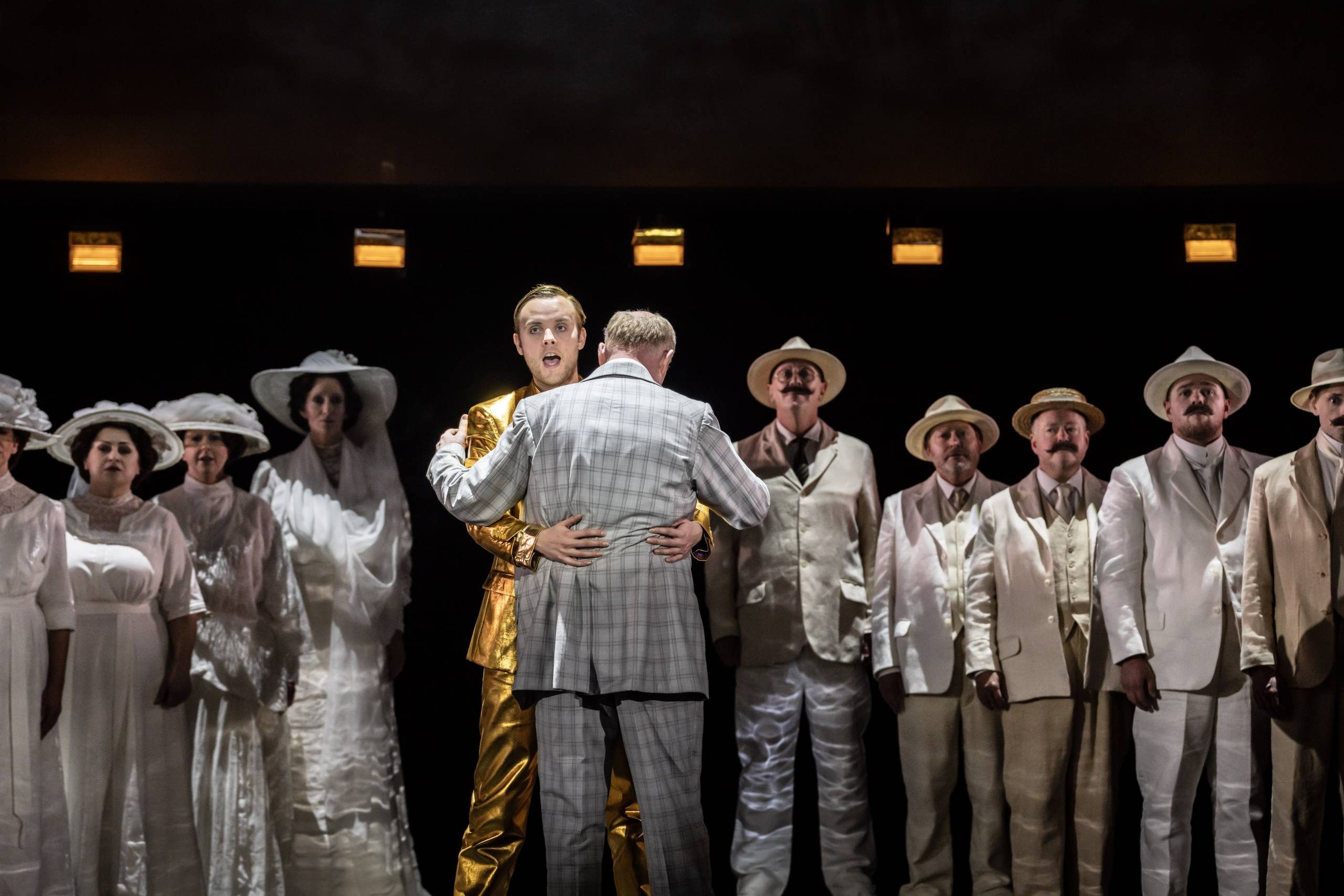 Apollo (Alexander Chance) hugs Aschenbach as the ensemble watches on.